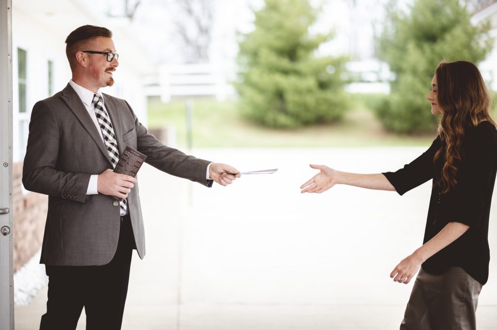 Shallow focus shot of a suited male handing religious brochures to a female wearing a skirt